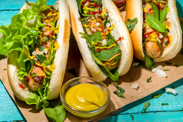 Homemade vegan hotdogs. Hot dog with white meat sausages, fresh vegetables, greens, sauces, over summer sun lighted blue wooden background copy space