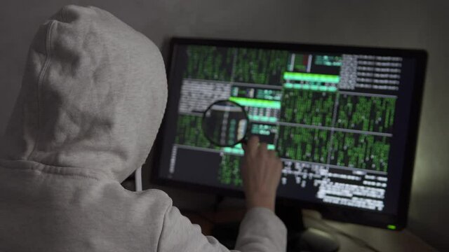 A scammer holds a magnifying glass and searches gullible internet users. Hacker tries to hack into the system