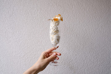 A glass with a festive sweet cocktail in the hands of a girl on a light background. Sweet dessert with cream and ice cream for the holidays. Celebrate and enjoy the moment. Glass close-up