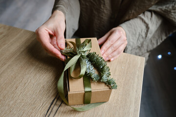 Woman holds a Christmas present in hands. Happy holiday, gift box close-up. Surprise for Boxing day, Christmas and New Year party. Celebration winter event. Wrapping paper, spruce branch and ribbon