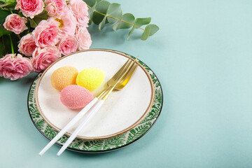  Table setting for celebrating easter. Plates, cutlery, colored eggs and spring pink flowers on the table