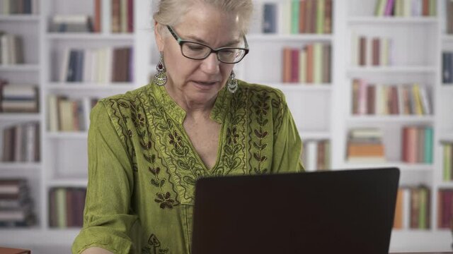 Camera pans down from woman smiling face to holding credit card and typing on laptop keyboard tas she makes online purchase.