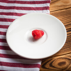A single raspberry on a white dish