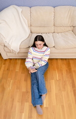 Top view of young teenage girl using smartphone browsing social media, shopping online sitting on the floor at home. 