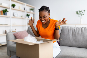 Overjoyed Afro woman unboxing carton parcel, emotional about successful shopping, satisfied with...