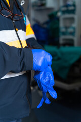 vertical photo of a paramedic putting on surgical gloves to attend an emergency. the ambulance is open behind him