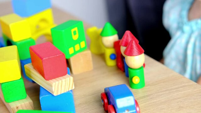 close-up of children's educational toys in hands of toddler, small child, a 2-year-old girl builds houses for characters from color blocks, concept of childhood, earlier child development, creativity