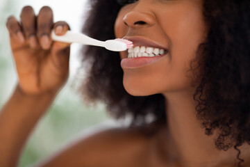 Dental hygiene concept. Cropped view of young black woman brushing her teeth indoors, closeup