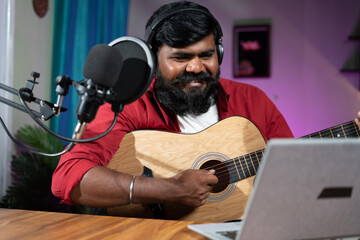 young beard mucisian teaching guitar through online class on laptop - concept of virtual training,...
