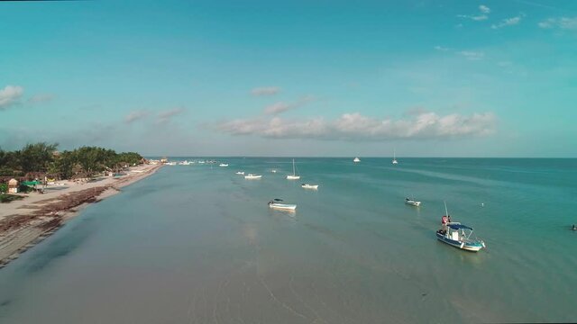 Local boats anchored in shallow water at shore of Holbox on sunny day, aerial