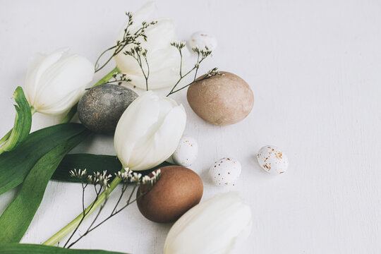 Happy Easter! Stylish Easter eggs and tulips on rustic white wooden background. Natural dyed eggs and spring flowers composition, tender atmospheric image. Greeting card