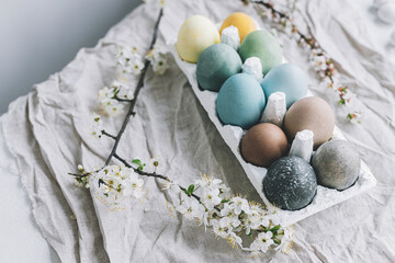 Stylish Easter eggs and cherry blossoms on rustic linen cloth. Happy Easter!  Natural dyed colorful pastel eggs in tray and spring flowers on rustic table. Countryside still life