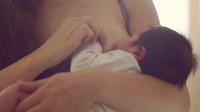 Mom breastfeeds a nursing baby. Close-up portrait of the infant and his mother. Window light.