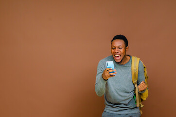 Over Excited cheerful dark skinned young man raises palm and stares overjoyed at smartphone display being social media blogger reads amusing article or watches funny video communicates online .