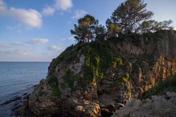 Fototapeta na wymiar Seascape. Mediterranean evening. Rocks surrounded by water on the beach protruding into the sea on a sunny day, Blanes, Catalonia, Spain.