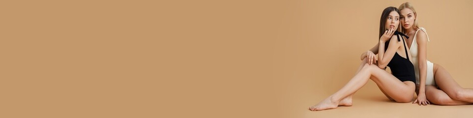 Sensual two women wearing swimsuits hugging while sitting on floor