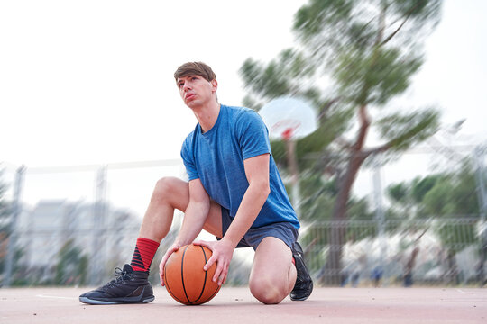 Detail shot of a young man holding a ball while kneeling on a basketball court.