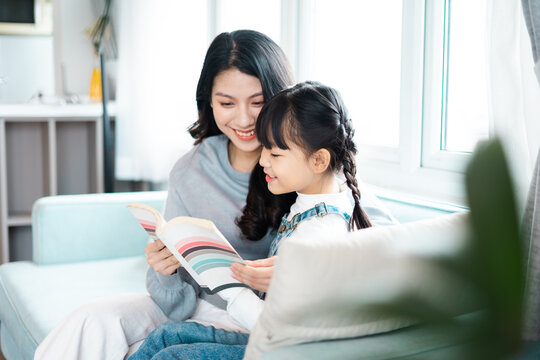 image of mother and daughter sitting on the sofa reading a book