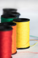 Spool of yellow tread with red and orange thread in foreground and green thread in background, white backdrop