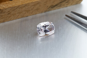 macro mineral faceted stone Morganite with tweezers on a gray background