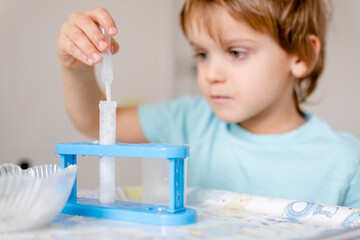 Happy boy in blue T-shirt conducts chemical experiments with vinegar and soda at home