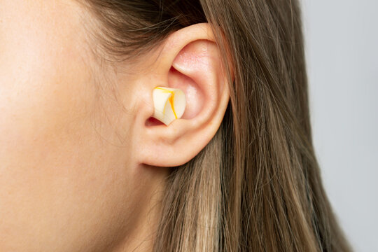 Close up of a young blonde woman's ear with polyurethane earplug isolated on a gray background. Anti-noise earbuds for sleep, rest, travel, airplane