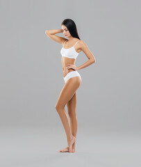 Fototapeta premium Attractive and slender brunette girl in white underwear posing in studio. Healthy lifestyle, sport and body care concept.