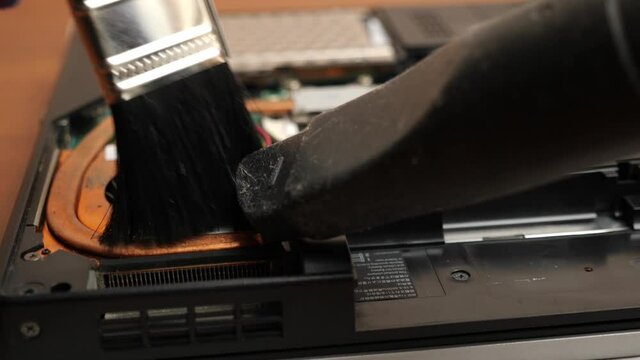 The wizard cleans the laptop's cooling system with a brush and a vacuum cleaner. PC care and repair concept.