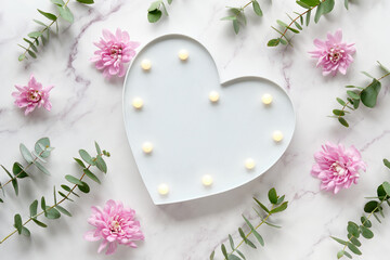 Heart shape lightbox. Winter flat lay with fragrant twigs and flowers. Wintertime eucalyptus, pink chrysanthemum flowers. Winter flat lay with fragrant evergreen plants. Top view on off white marble.