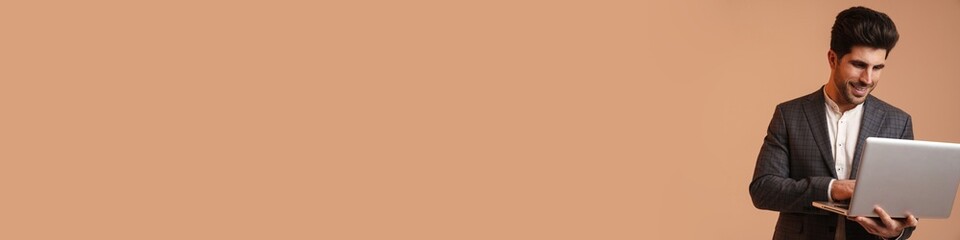 Smiling young man in jacket standing while working with laptop