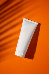 Plastic white bottle for cream or lotion on a orange background. Skincare cosmetic with beautiful palm shadows. Beauty concept for face body care.