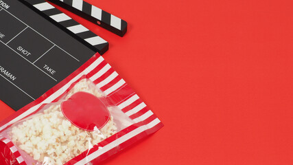 Black clapper board or movie slate and red pop corn bag on red background.