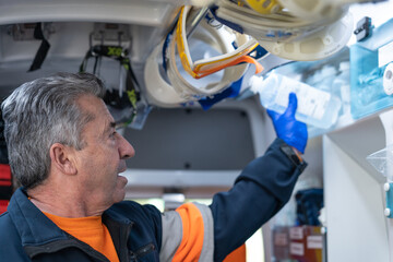 photo of a middle-aged paramedic with white hair taking out a bottle of physiological serum from an ambulance compartment