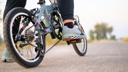 Fototapeta na wymiar Closeup woman going to ride the folding bike in countryside to exercise, closeup in low angle shot at her foot that rest on the pedal