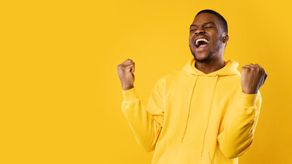 Emotional Black Man Shouting Shaking Fists Celebrating Success, Yellow Background