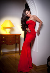 The beautiful girl in a long red dress posing in a vintage scene.Young beautiful woman wearing a...