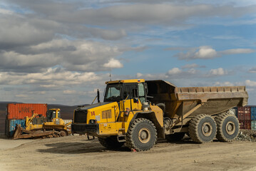 An articulated dump truck waiting to be repaired stands near the containers at the gold mine site.