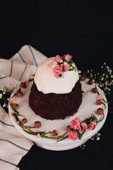 Easter cake with white icing decorated with flowers on a white stand on a black background.