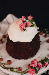 Easter cake with white icing decorated with flowers on a white stand on a black background.