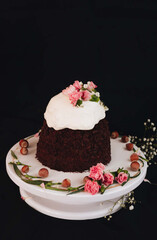Easter cake with white icing decorated with flowers on a white stand on a black background.