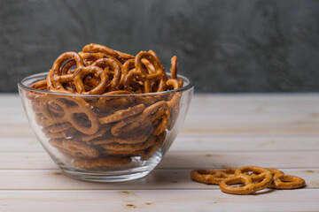 Salted mini pretzels in a deep glass bowl on a wooden tabletop. Popular beer snack. Space for text.