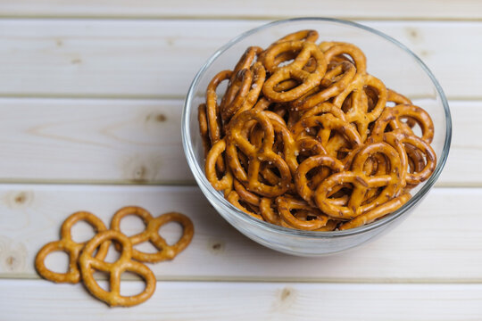 Salted mini pretzels in a deep glass bowl on a wooden tabletop. Popular beer snack.