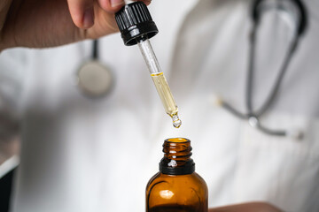 Male Caucasian doctor hands opening a glass pipette bottle and dropping droplets of CBD hemp oil, close-up shot.