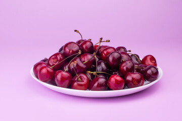 Sweet red cherry on white ceramic plate on pink background.