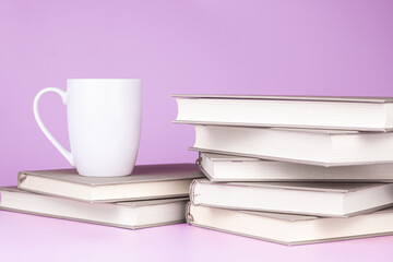 White cup with coffee or tea is on stack of books on pink background. Education mock up concept with copy space.