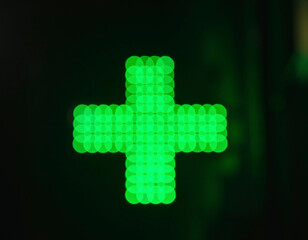 Świecący, zielony krzyż równoramienny oznaczający miejsce położenia apteki. - obrazy, fototapety, plakaty