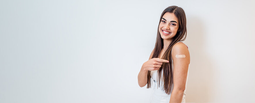 Young Girl Woman Showing Pointing With Finger To Bandage On Her Arm Shoulder Cheerful Happy And Smiling Done With Vaccination. Female Just Got Vaccinated Against Covid19 Face Mask Looking At Camera.