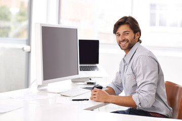 This is easy. A young businessman sitting at his desk and smiling at the camera.