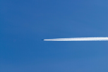 Samolot lecący na błękitnym niebie, pozostawiając za sobą białą smugę kondensacyjną. - obrazy, fototapety, plakaty