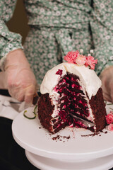 A female with gloved hands cuts an Easter cake with cherry cream and white icing, decorated with flowers.
